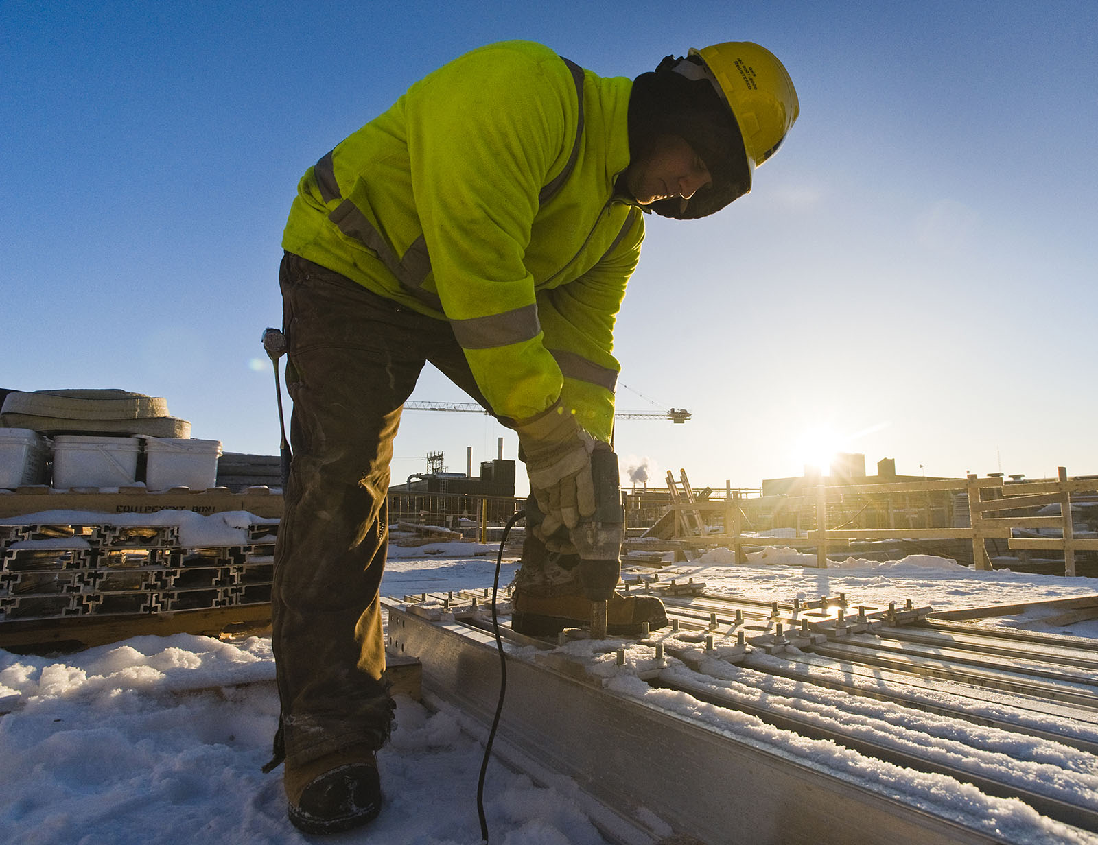 A person working outside in the sun with a drill machine.