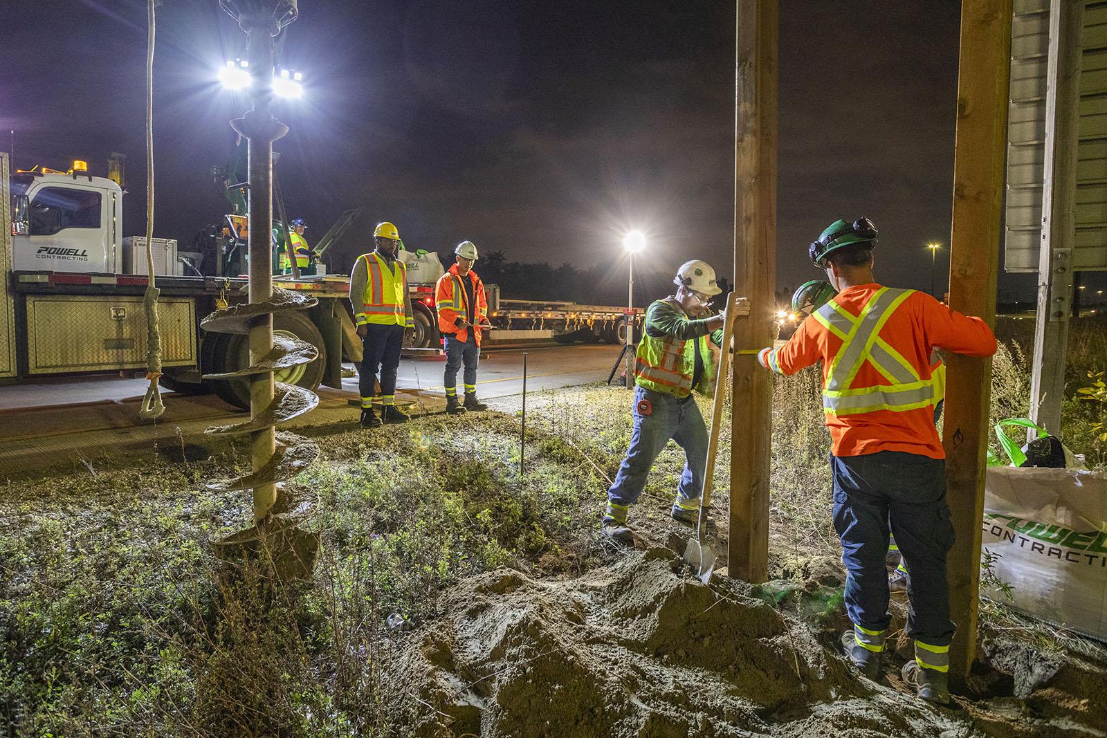 Image of construction workers at night, planting structural components in the ground.