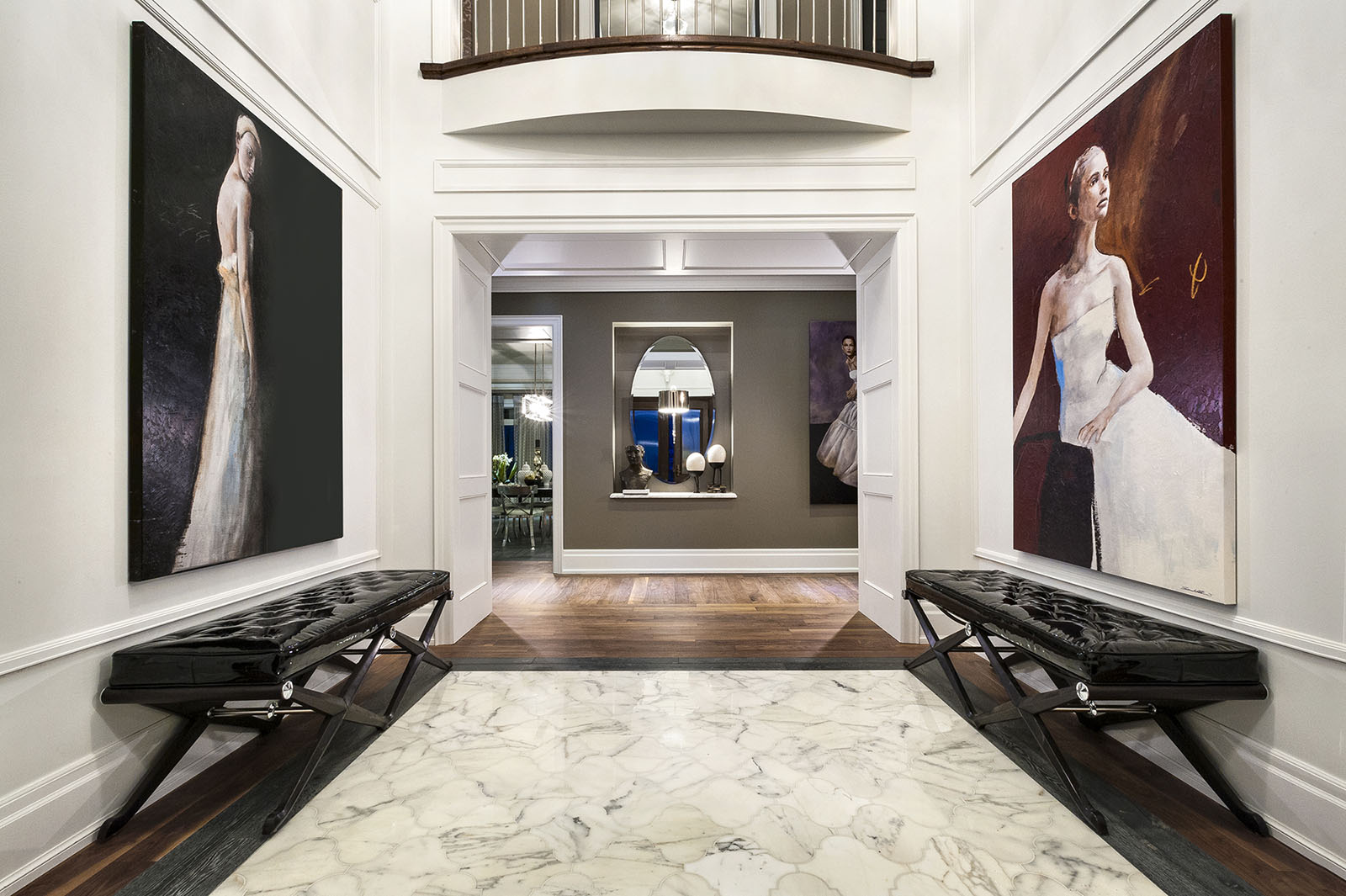 Symmetrical image of a residence’s entrance area with marble flooring, two paintings on the side walls, and two ottomans placed by them.