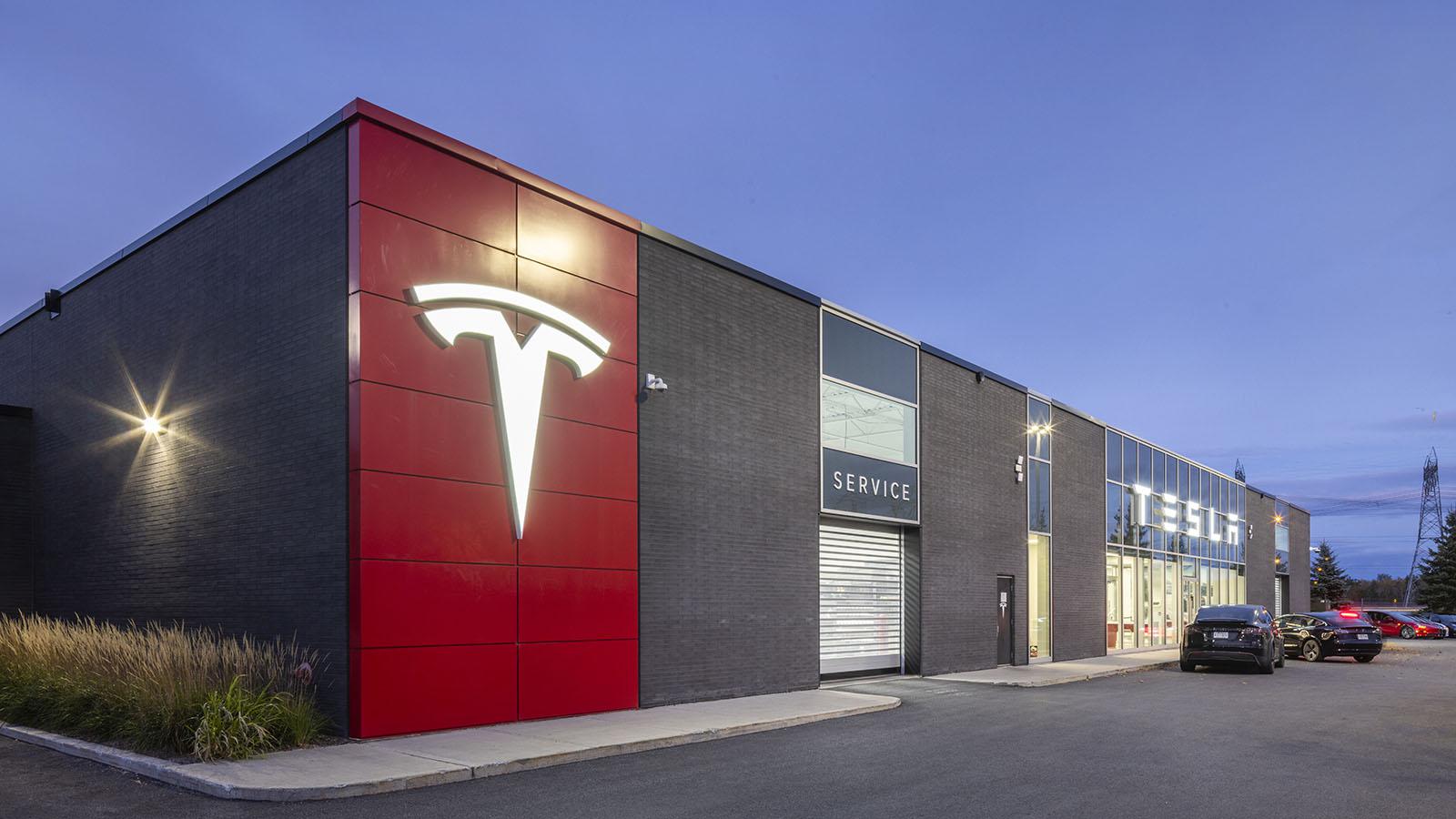 Image of a red and grey building with cars in the distance.