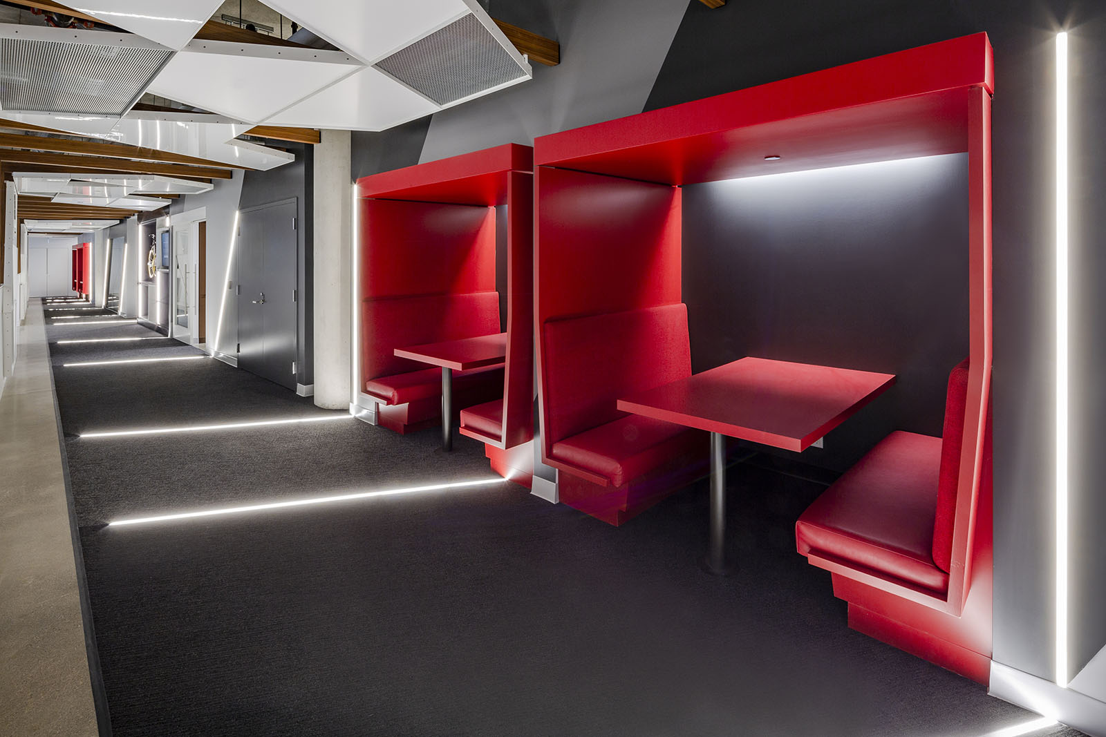 Corporate office photography of a modern breakout lounge with red booth seating and LED accent lighting.